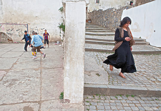 Usando arcos pintados, un grupo de niños juega en una pequeña plaza mientras una mujer desciende por una de las calles pavimentadas en piedra de la parte alta de la Casbah, donde la calle más empinada posee 472 escalones.
