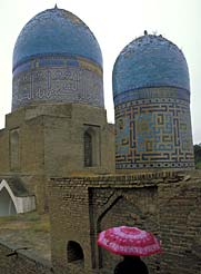 A red umbrella contrasts colorfully with Samarkand's blue-tiled domes