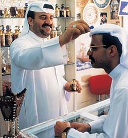 A Bahraini shopkeeper daubs a gentleman’s blend on the top of a customer’s <em>ghutra</em> in the traditional fashion. 