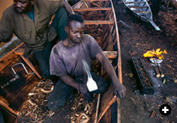 A boatwright on Mopti's waterfront shapes the casedral woodwork of a new pinasse with an adze. 