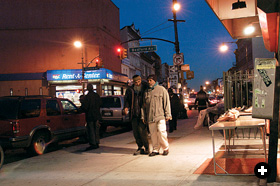 Two recent immigrants, one now a local shop-owner, walk past the Bedford Avenue corner. 