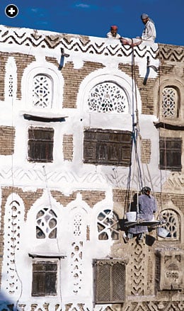 Suspended on a seat called an isqalah ("cradle"), a crafstman applies gos, a white gypsum slurry, around windows. 