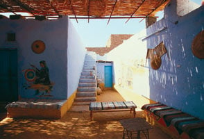 Nubian houses today increasingly resemble Arab ones in the use of separate men’s and women’s rooms built off a central shaded courtyard. Both painted and three-dimensional objects, here fans and baskets woven of palm fronds, are part of the decoration.