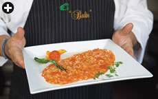 Balin’s tomato risotto is a refinement of an essentially simple process: The rice is first sautéed in butter, and then cooked by boiling it in a small amount of stock and—depending on the risotto—a few or many other ingredients. As the liquid begins to be absorbed by the rice, a bit more is stirred in, and so on until the rice is cooked and the flavors of the liquid have been absorbed.