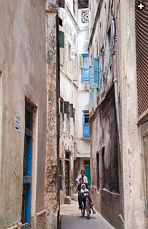 In Stone Town, children ride through a narrow street. 