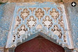 Seven medallions, framed by floral and shell motifs, decorate a carved and painted panel above a doorway. The medallions on the panels flanking it repeat “[there is] no victor but God.”