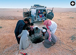 Interested spectators watch as a caver rigs for descent into a dahl, or sinkhole, in the limestone plateau near Ma’aqalla. Only a small percentage of dahls lead to dry caves, most are simply plugged by wind-blown sand.